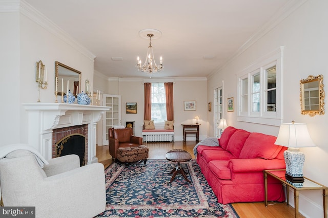living area with crown molding, wood finished floors, radiator heating unit, a brick fireplace, and an inviting chandelier