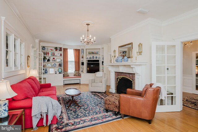living room featuring an inviting chandelier, ornamental molding, a fireplace, and wood finished floors