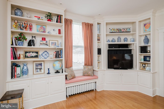 sitting room with radiator, crown molding, light wood finished floors, and built in shelves