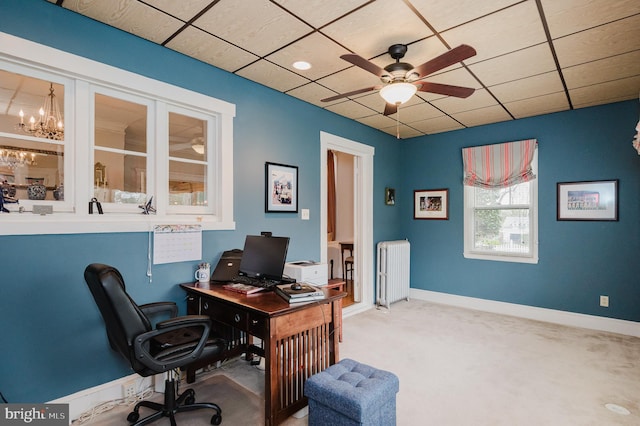 office space featuring carpet flooring, ceiling fan with notable chandelier, baseboards, radiator heating unit, and a paneled ceiling