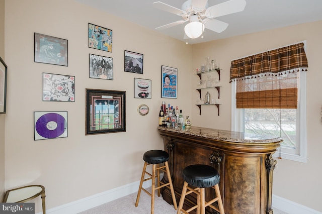 bar with a bar, baseboards, and ceiling fan
