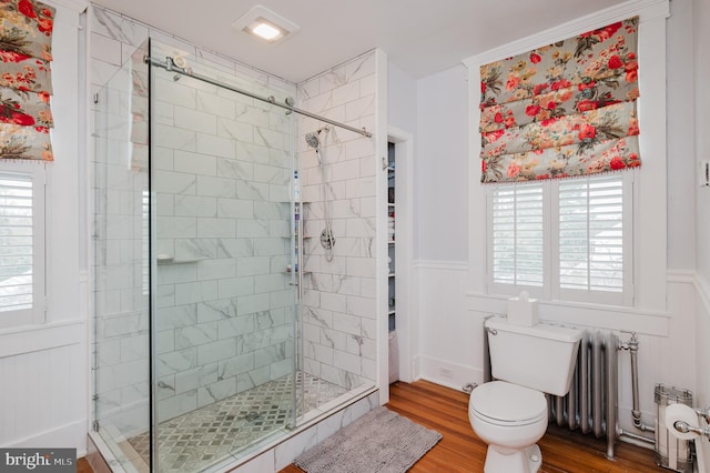 bathroom with a stall shower, a wainscoted wall, toilet, wood finished floors, and radiator heating unit