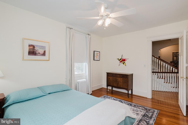 bedroom with radiator, baseboards, arched walkways, and wood finished floors