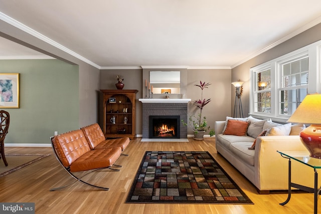 living room with baseboards, wood finished floors, ornamental molding, and a brick fireplace