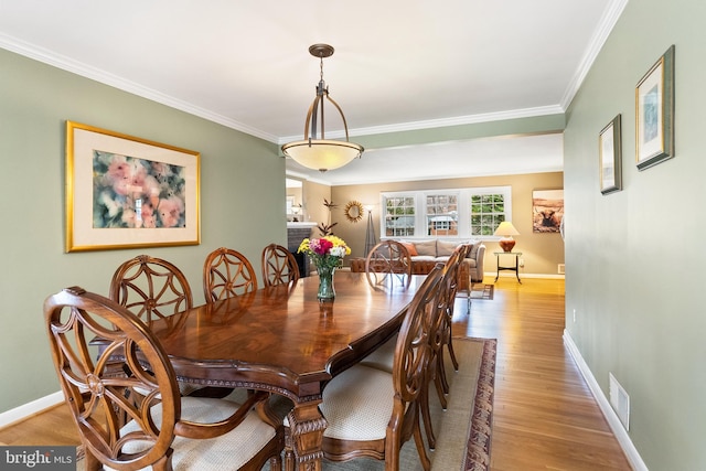 dining area featuring light wood finished floors, baseboards, visible vents, and crown molding