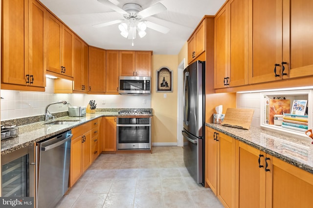 kitchen featuring a sink, a ceiling fan, light stone countertops, stainless steel appliances, and decorative backsplash