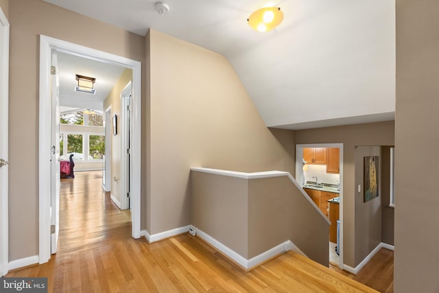 corridor featuring an upstairs landing, light wood finished floors, baseboards, lofted ceiling, and a sink