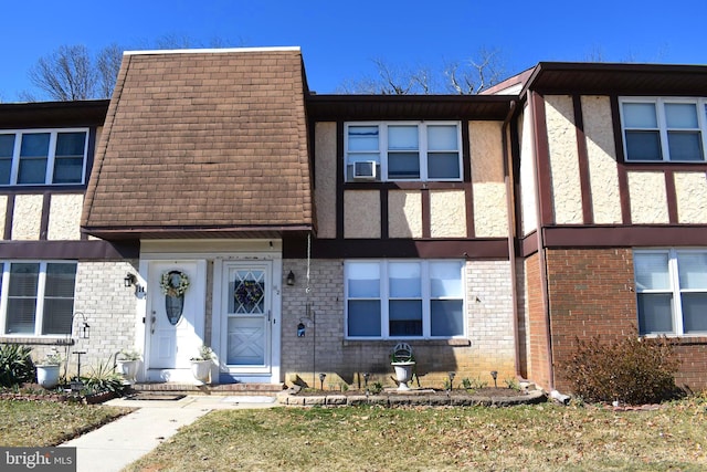 view of front of property featuring brick siding, stucco siding, mansard roof, and a shingled roof