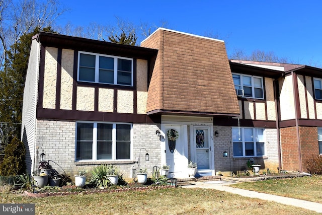 view of front facade with a front yard, brick siding, roof with shingles, and mansard roof