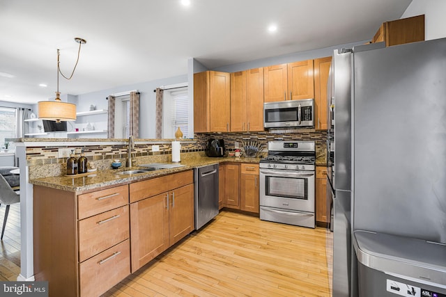 kitchen featuring stainless steel appliances, light wood-style flooring, decorative backsplash, a sink, and a peninsula