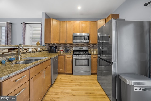 kitchen featuring stainless steel appliances, backsplash, stone countertops, light wood-style floors, and a sink