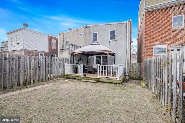 back of house with stucco siding, a wooden deck, a fenced backyard, and a gazebo