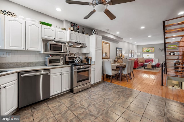 kitchen with light tile patterned flooring, under cabinet range hood, stainless steel appliances, white cabinetry, and decorative backsplash