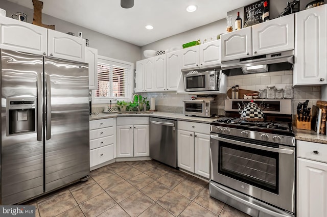 kitchen with under cabinet range hood, stainless steel appliances, a sink, white cabinetry, and backsplash