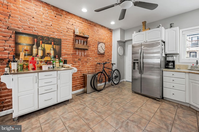 kitchen featuring white cabinetry, stainless steel refrigerator with ice dispenser, brick wall, and light tile patterned flooring