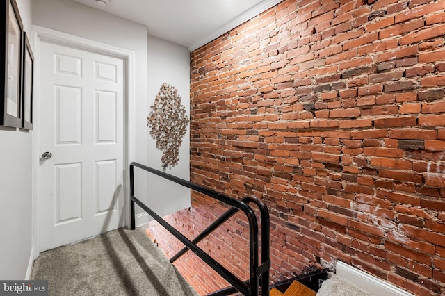 staircase with brick wall and carpet flooring