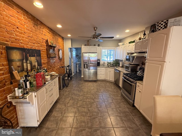 kitchen featuring recessed lighting, brick wall, stainless steel appliances, a sink, and white cabinets