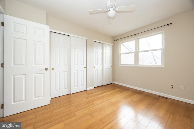 unfurnished bedroom featuring baseboards, light wood-style floors, visible vents, and multiple closets