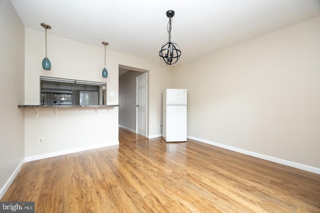 unfurnished living room featuring a notable chandelier, baseboards, and wood finished floors