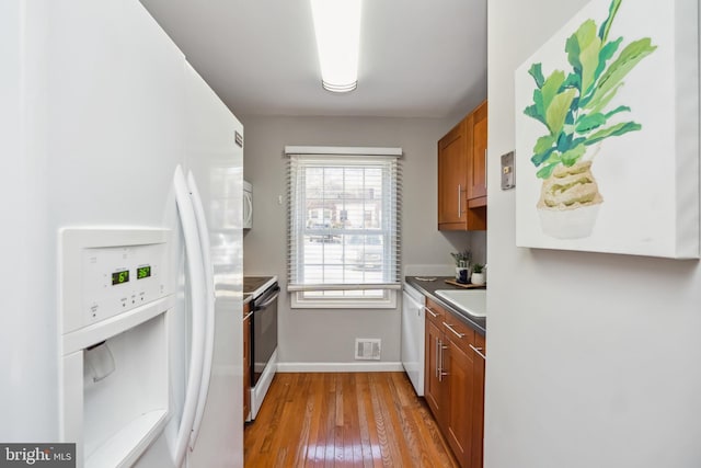 kitchen with white appliances, visible vents, brown cabinets, and wood finished floors