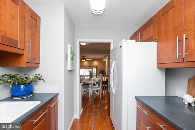 kitchen featuring ceiling fan, dark wood-style flooring, freestanding refrigerator, brown cabinets, and dark countertops