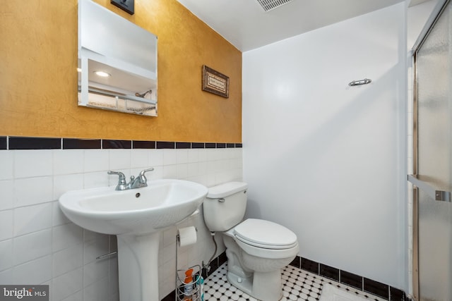 full bath with toilet, a stall shower, tile walls, and tile patterned floors