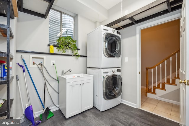 clothes washing area with cabinet space, a sink, stacked washer and clothes dryer, and baseboards