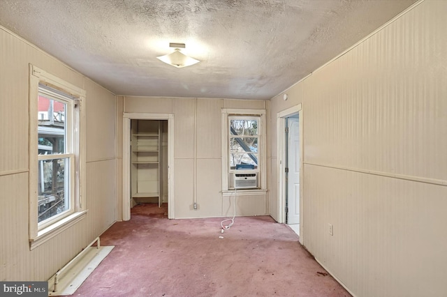 unfurnished bedroom with a textured ceiling, multiple windows, cooling unit, and carpet flooring