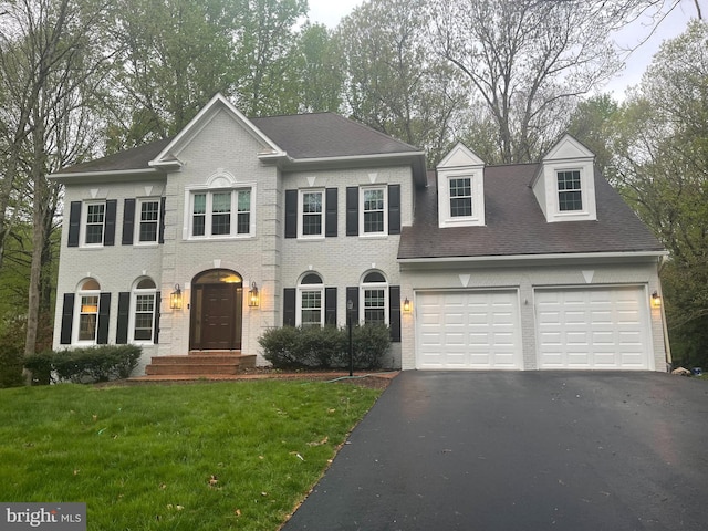 colonial inspired home featuring aphalt driveway, brick siding, an attached garage, and a front lawn