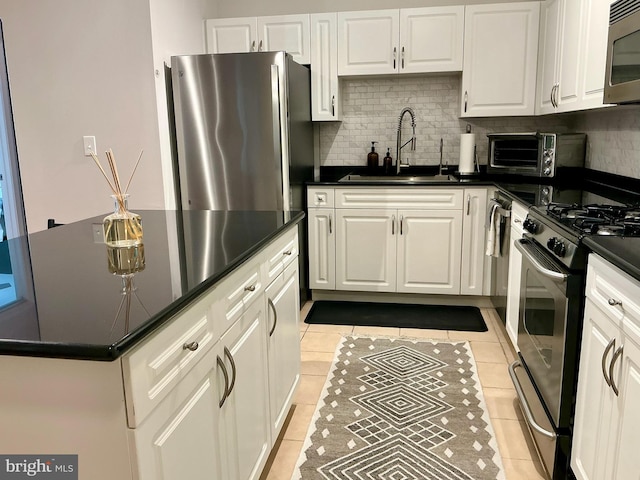 kitchen featuring stainless steel appliances, dark countertops, a sink, and white cabinetry