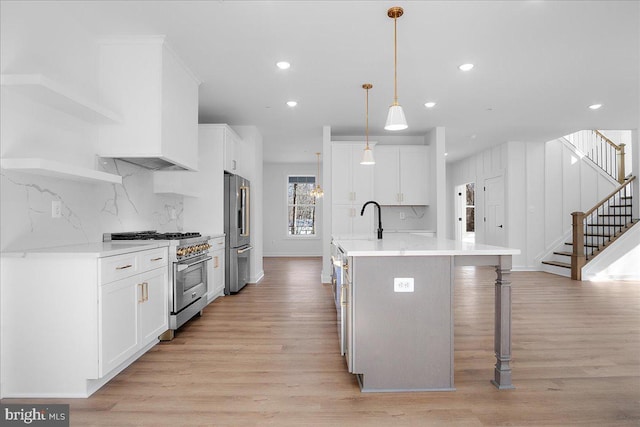 kitchen featuring a sink, light wood-style floors, open shelves, high end appliances, and a center island with sink