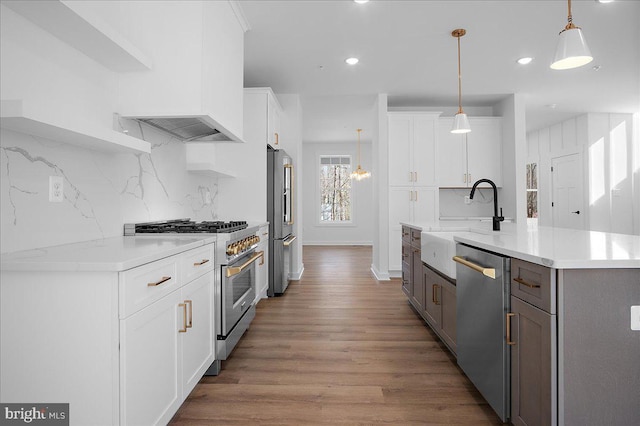 kitchen with premium appliances, pendant lighting, white cabinets, a sink, and wood finished floors