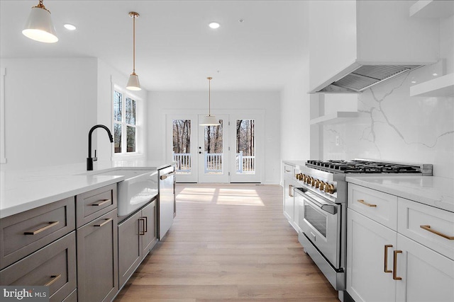 kitchen with stainless steel appliances, custom range hood, backsplash, light wood-style floors, and a sink