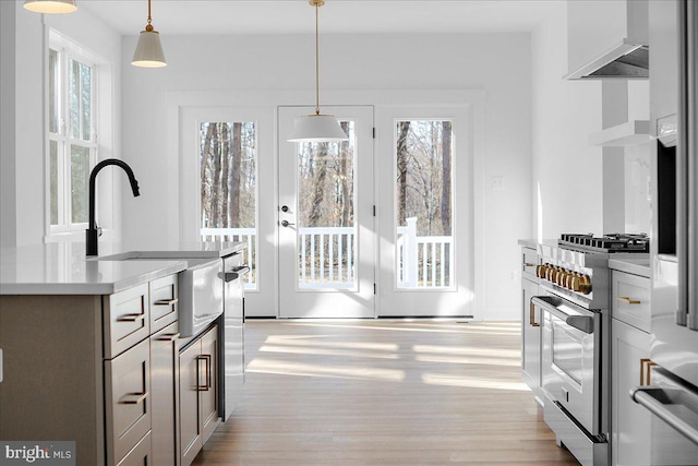 kitchen featuring light countertops, hanging light fixtures, light wood finished floors, and high end stainless steel range