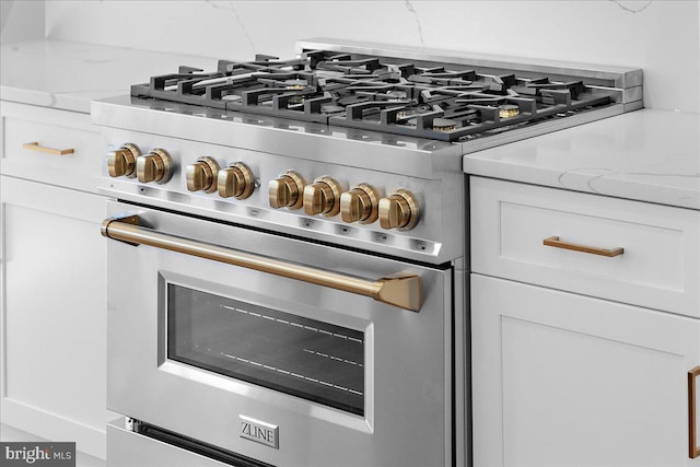 room details featuring high end stainless steel range, light stone countertops, and white cabinets