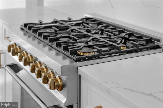 room details featuring light stone countertops, stainless steel stove, and white cabinets