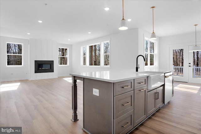 kitchen featuring gray cabinets, a kitchen island with sink, light wood-style flooring, and stainless steel dishwasher