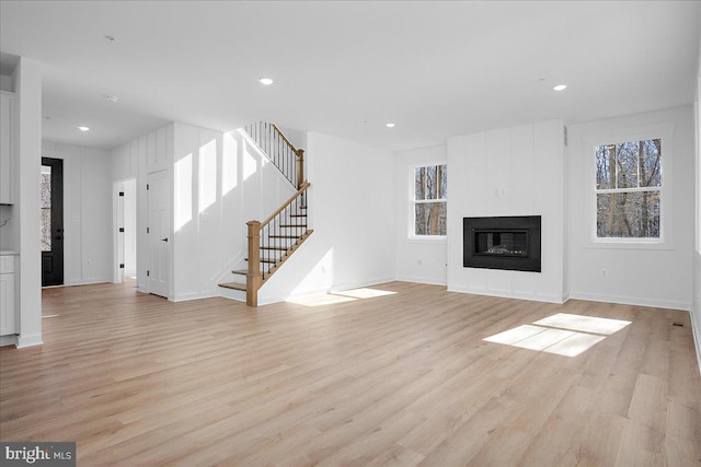 unfurnished living room with light wood-type flooring, stairs, a fireplace, and recessed lighting