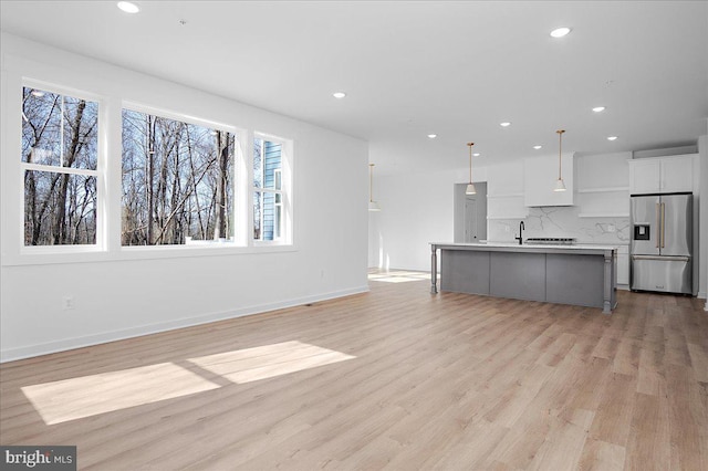 kitchen with light wood-style flooring, white cabinets, stainless steel refrigerator with ice dispenser, decorative backsplash, and pendant lighting