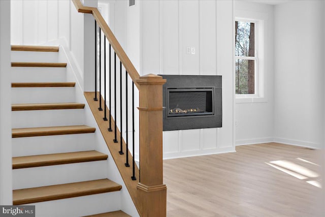 stairs with baseboards, wood finished floors, and a glass covered fireplace