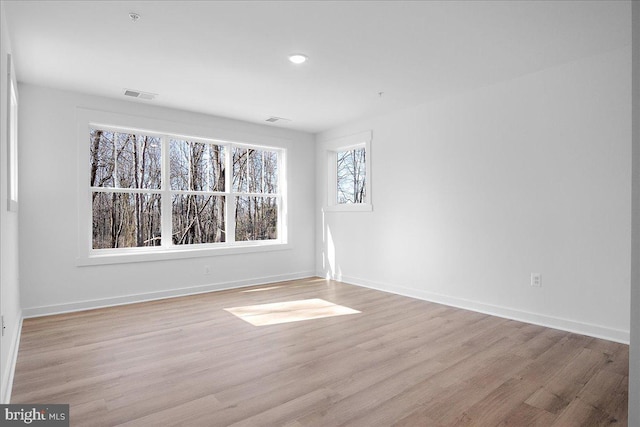 empty room with light wood-style floors, visible vents, and baseboards