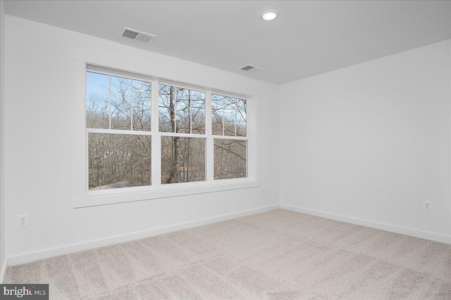 empty room featuring a wealth of natural light, carpet, visible vents, and baseboards