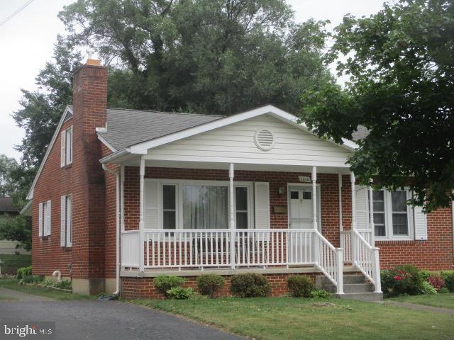 view of front of home featuring a front yard, covered porch, brick siding, and a chimney