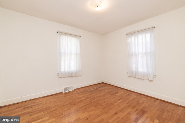 unfurnished room featuring a healthy amount of sunlight, visible vents, light wood-style flooring, and baseboards