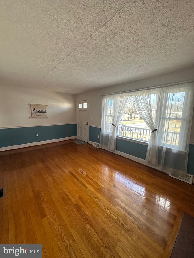 unfurnished living room featuring a textured ceiling, wood finished floors, visible vents, and baseboards