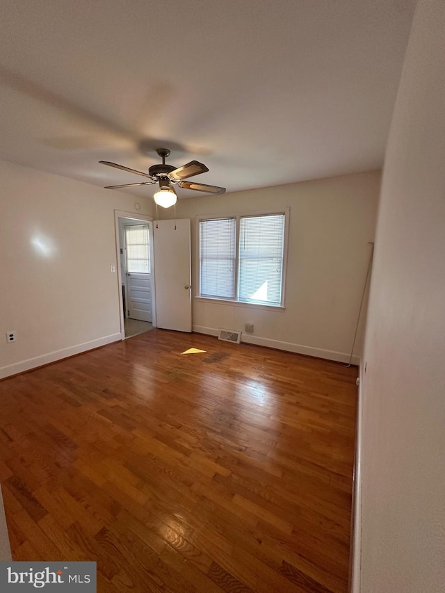 empty room with a ceiling fan, visible vents, baseboards, and wood finished floors