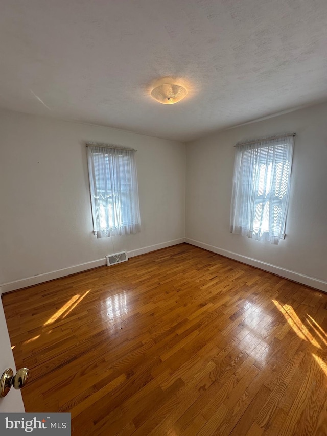 spare room featuring plenty of natural light, visible vents, wood-type flooring, and baseboards