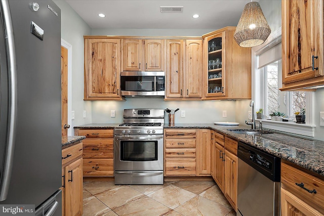 kitchen featuring appliances with stainless steel finishes, dark stone countertops, a sink, and visible vents