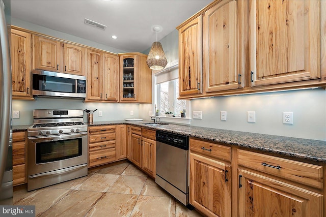 kitchen featuring visible vents, appliances with stainless steel finishes, glass insert cabinets, a sink, and dark stone countertops