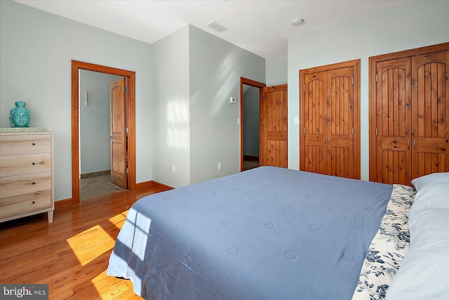 bedroom with visible vents, two closets, baseboards, and wood finished floors